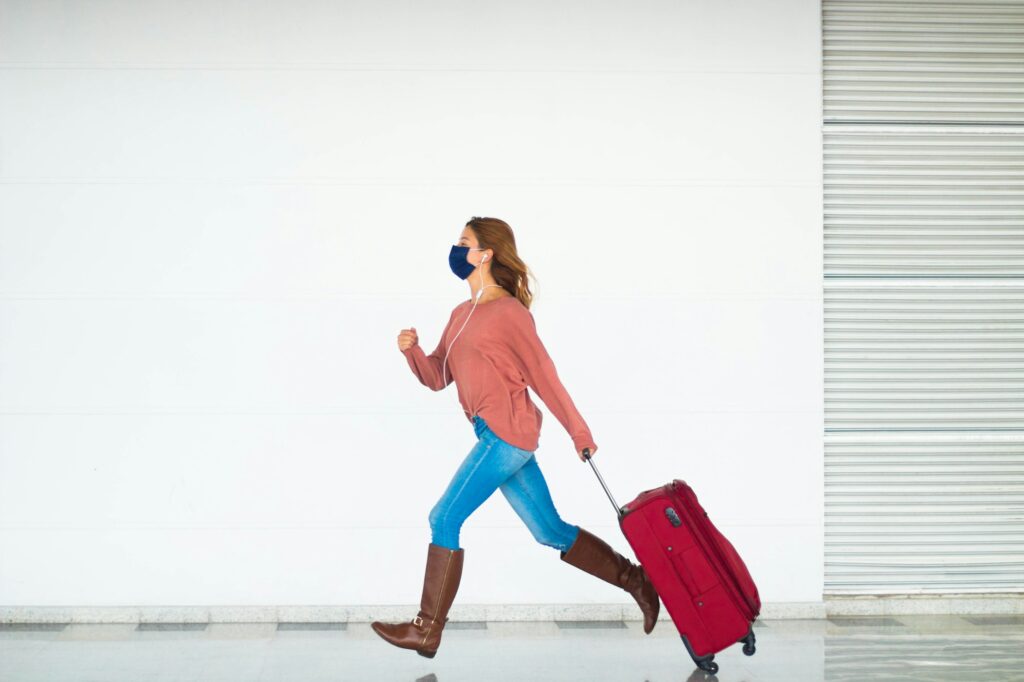 Woman wearing a facemask holding a suitcase running late for her flight